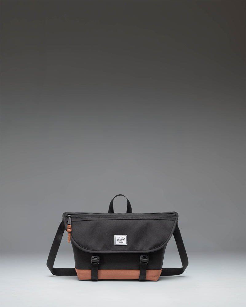 Herschel Supply Co. Cove Small Messenger bag in Black and Saddle Brown, showcasing a compact crossbody design with an adjustable shoulder strap.