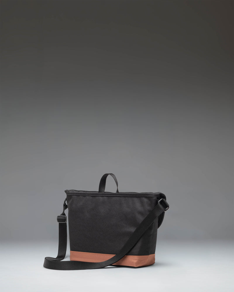 Herschel Supply Co. Cove Small Messenger bag in black with a saddle brown base and strap detailing, shown from a front angle.
