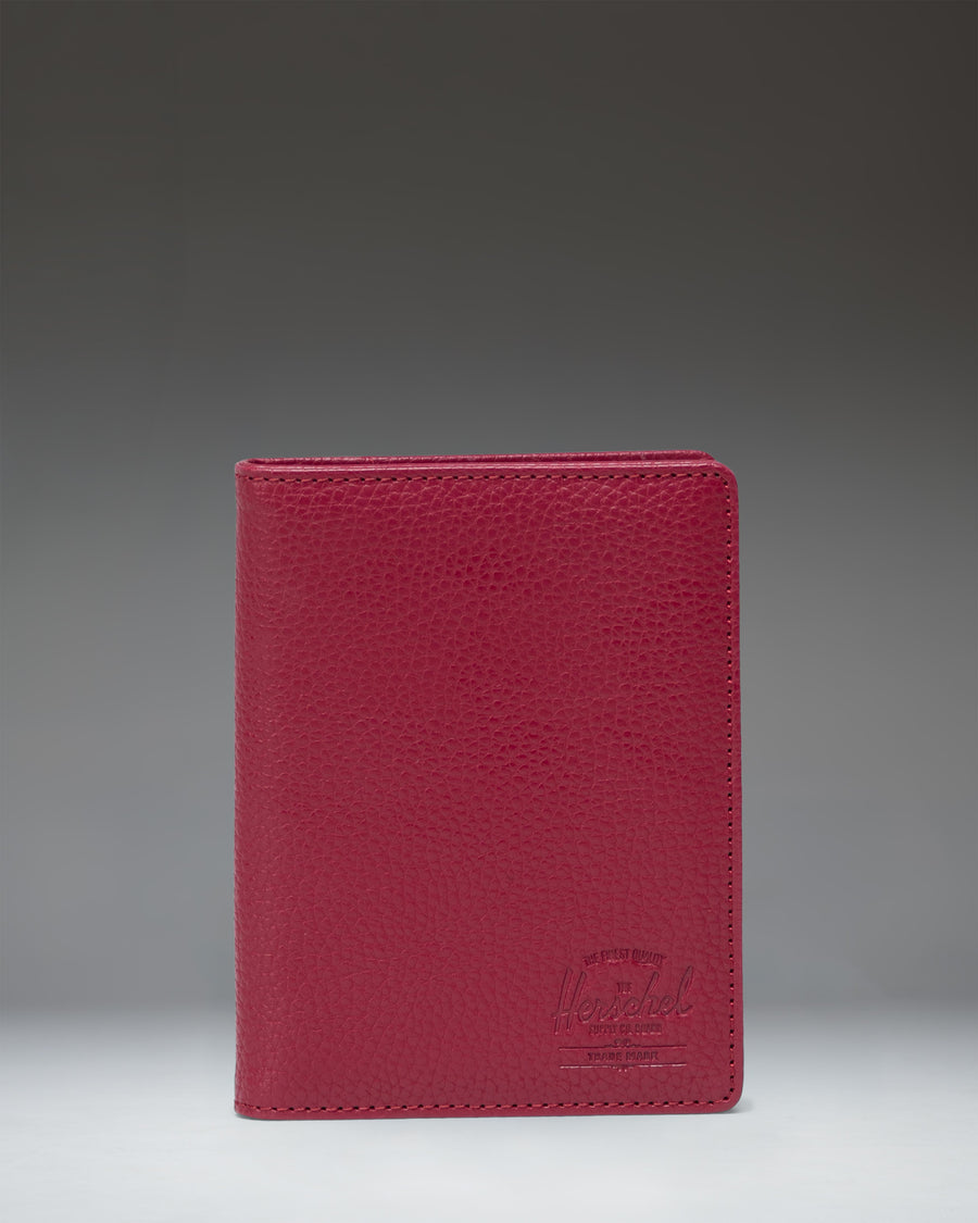 Herschel Supply Co. Raynor Passport Holder in Cherry Red vegan leather, showing its textured finish and sleek, minimalist design.