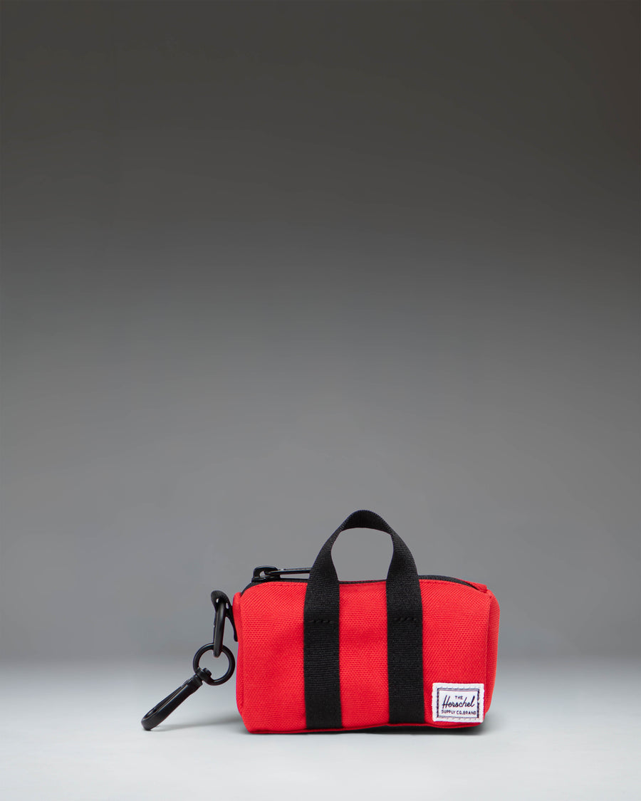 Herschel Novel Duffle Bag Charm in Bright Red, showcasing a miniature duffle bag design with carrying handles and a clip attachment.