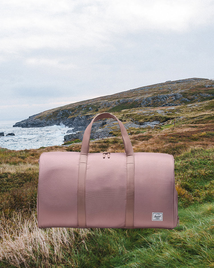 Herschel Novel Duffle bag in Ash Rose pink, featuring a classic duffle silhouette with top handles and a shoulder strap.