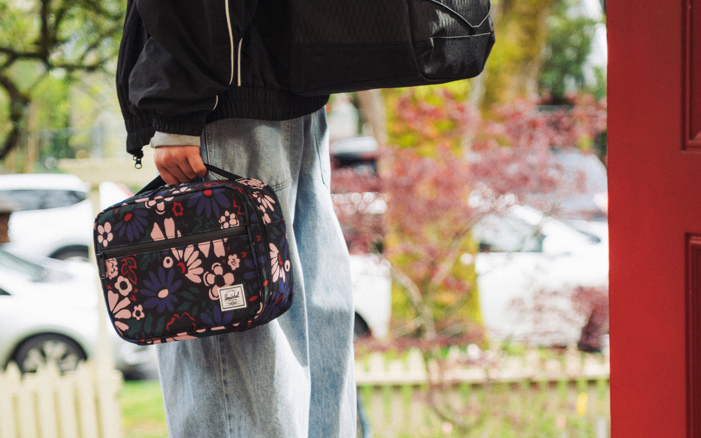 Herschel Supply Co. Pop Quiz insulated lunch box in Moody Bloom, featuring a dark floral pattern with a front zip pocket and top handle.