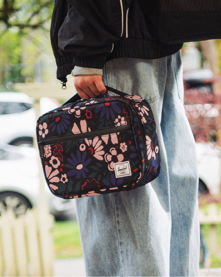 Herschel Pop Quiz Lunch Box in Moody Bloom, featuring a dark floral pattern with a front storage pocket and top carrying handle.