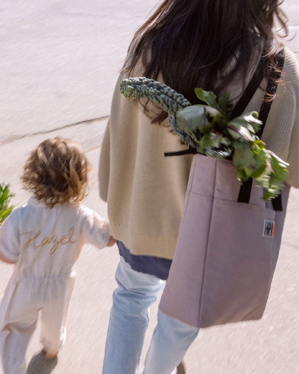 une femme avec un sac cabas rempli de légumes marche avec sa petite fille.