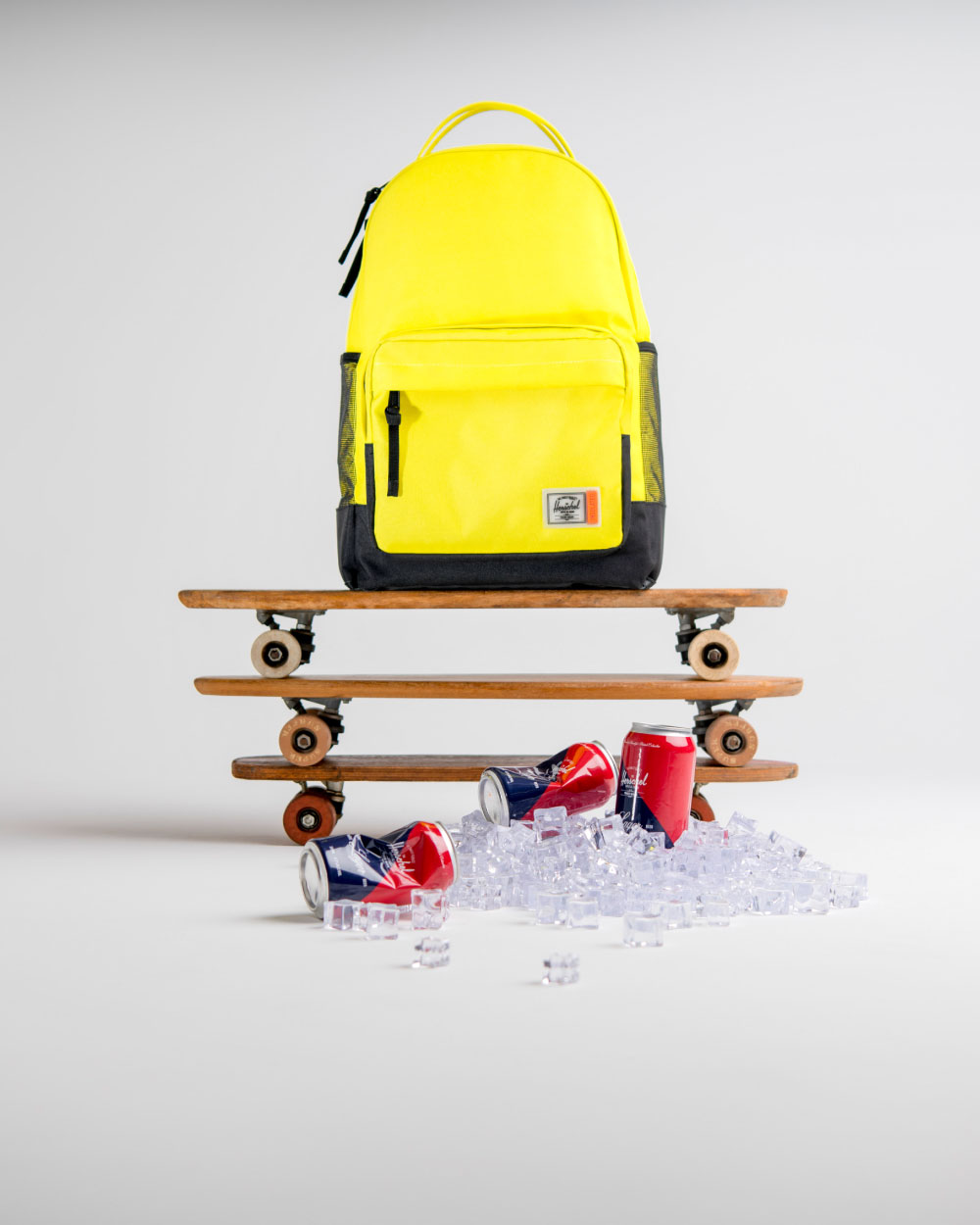 A Herschel Supply Miller Backpack Insulated in Sulphur Springs on top of 3 skateboards stacked on top of one another with some loose ice & empty cans in front of it.