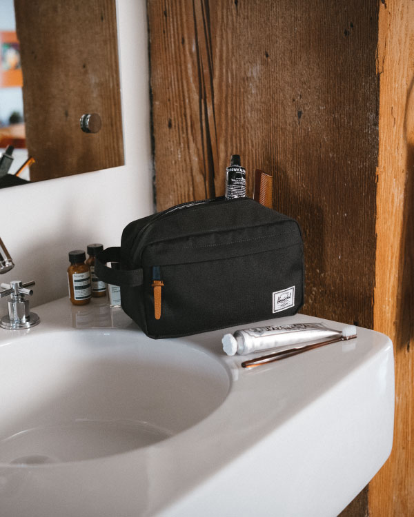 A black Chapter Travel Kit on the side of a sink with toiletries laid out around it.