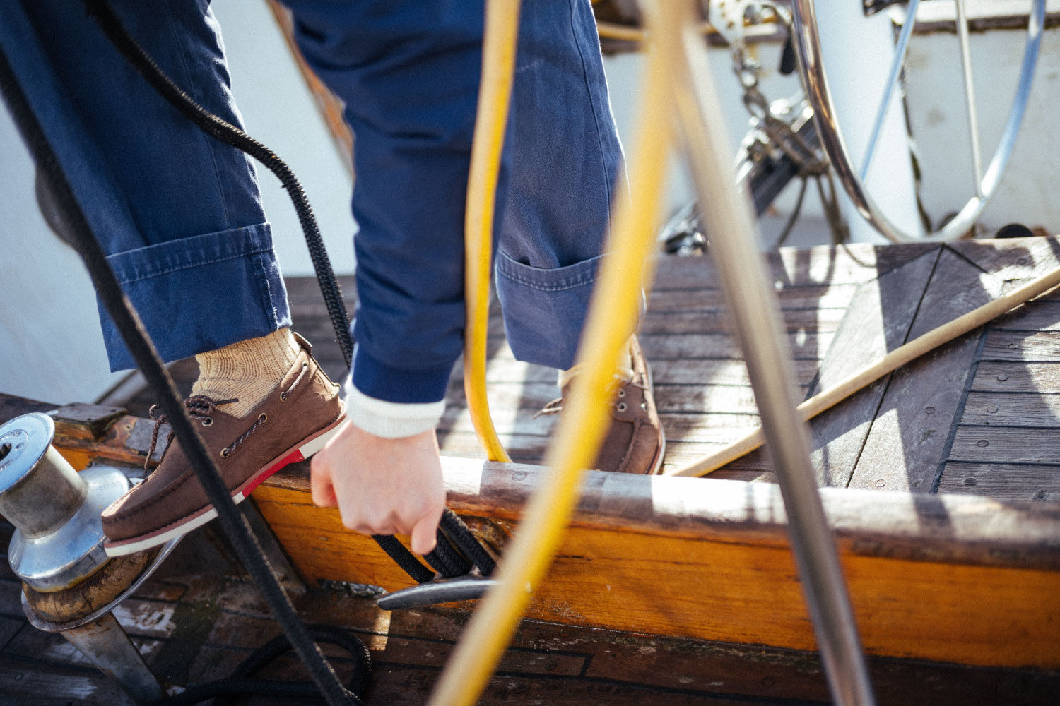 A person tying a sailboat up to the dock wearing the Herschel Supply Company x Sperry Authentic Original Lug Chukka shoes in Brown/Blanc de Blanc