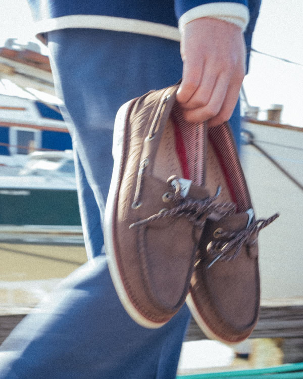 A person walking along a dock beside a sailboat with the Herschel Supply Company Authentic Original Lug Chukka Sperry shoes in Peacoat/Navy/Blanc de Blanc
