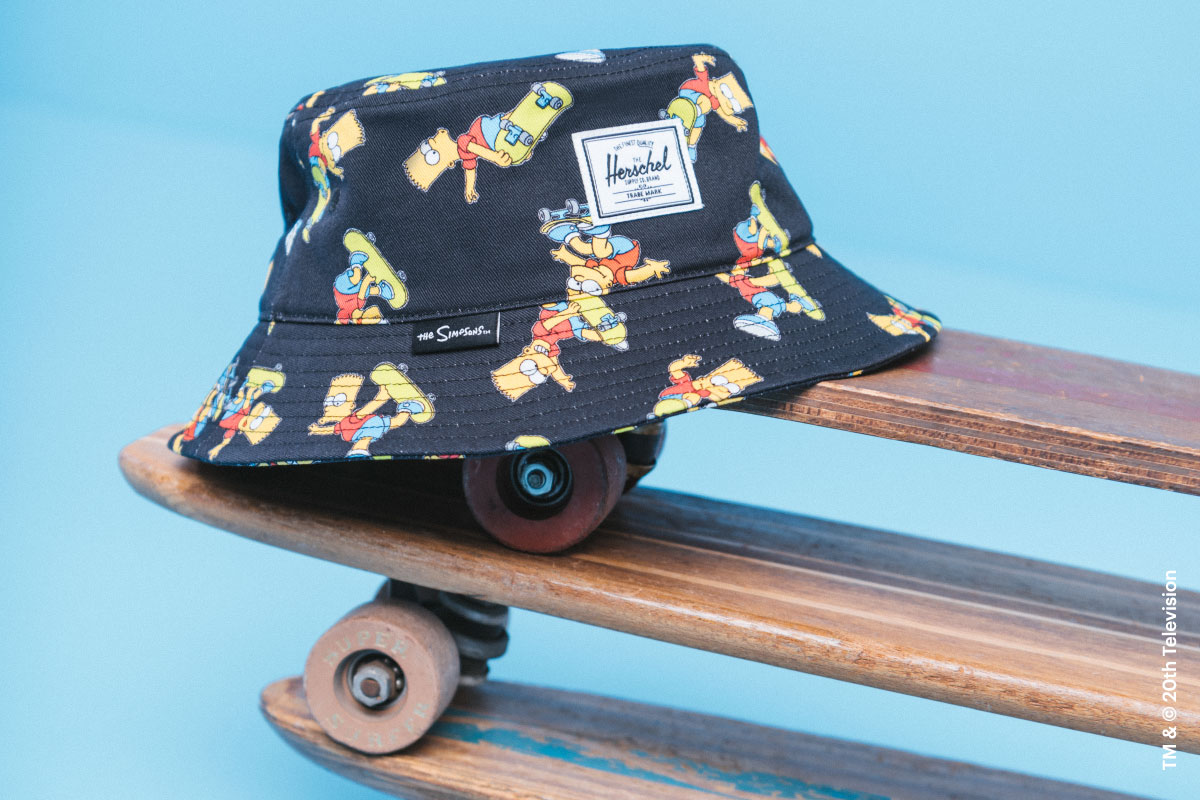 The Norman Bucket Hat in Bart Simpson print on a stack of skateboards with the Herschel Supply Company label on the front of the hat