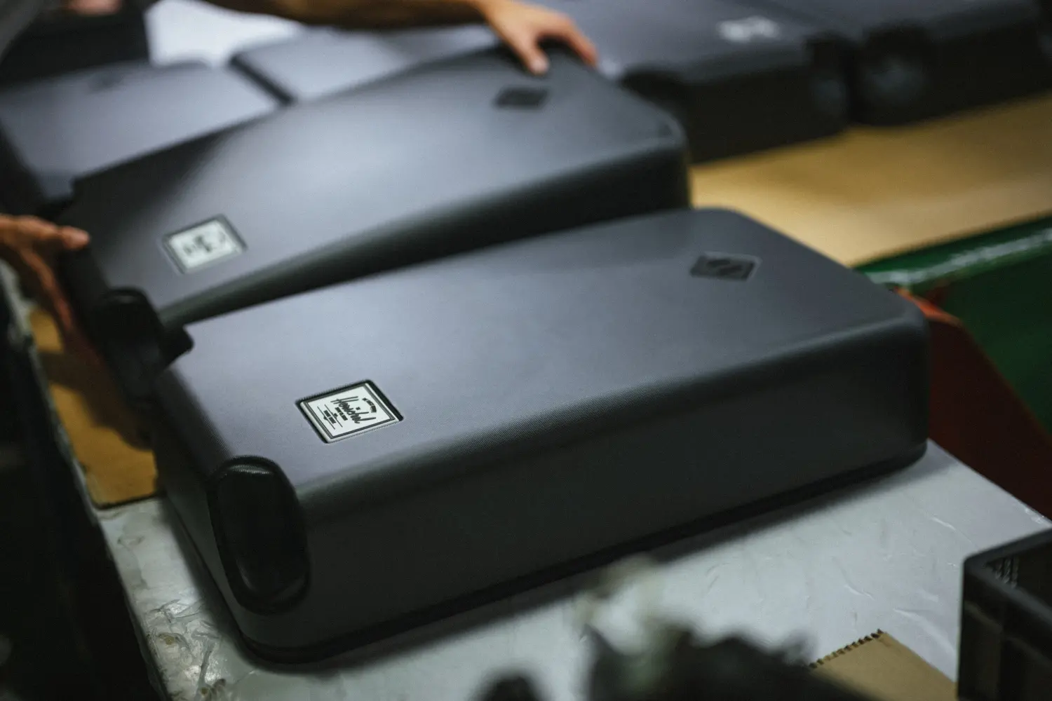 An image of a row of hardshell luggage exteriors being inspected by a worker.