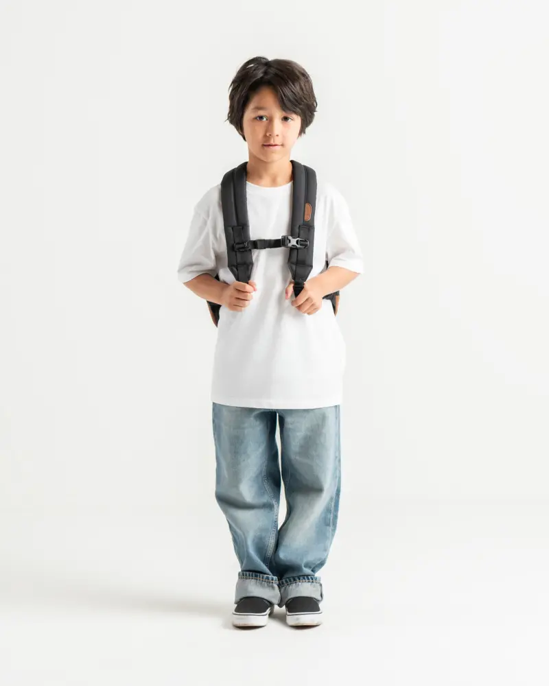 a child stands in front of a white background with a black heritage youth backpack on 