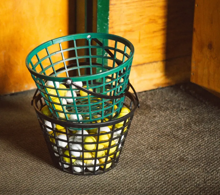 Two buckets of golf balls from a driving range stacked on top of each other with a few golf balls in each