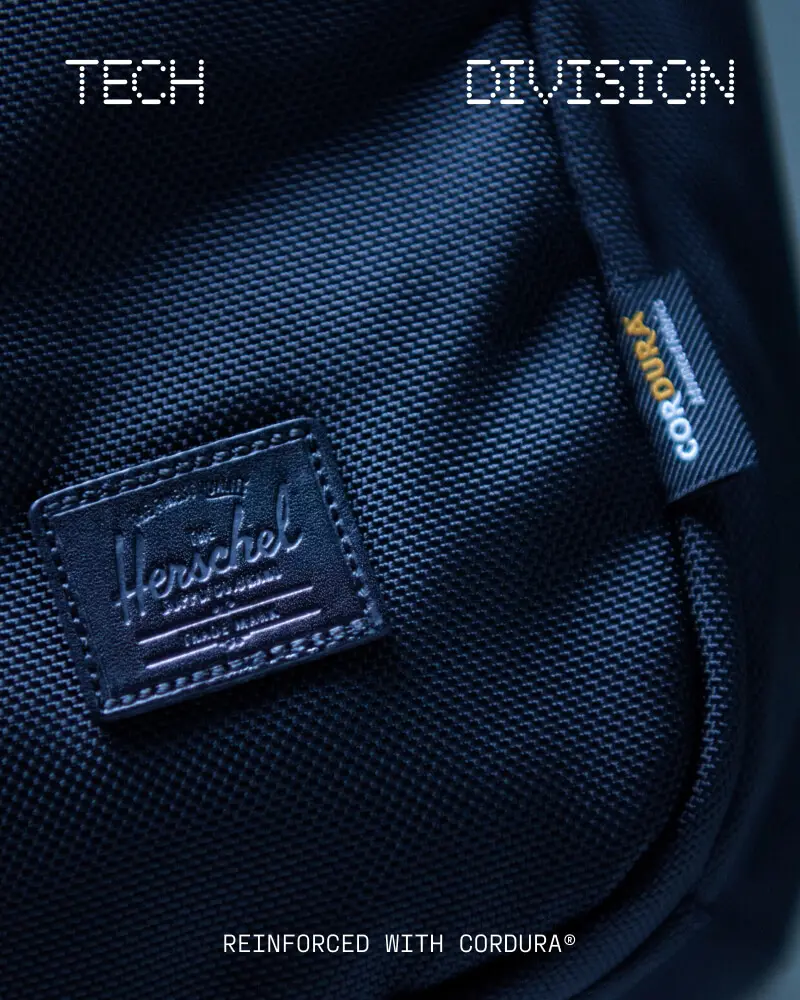 An image of a man standing in the rain, waiting for a bus, wearing a black Herschel Alberni Weather Resistant Backpack 