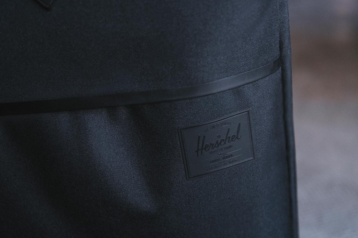 The front zippered pocket of the Highland Luggage Carry-On Large with the tonal black Herschel Supply Company label